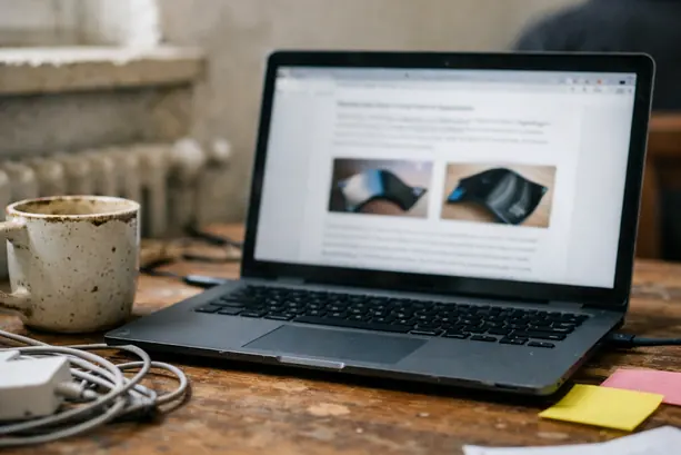 Home office writing setup with laptop on a slightly scuffed wooden desk, screen open